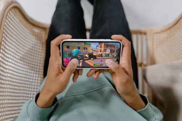 Isang pares ng mga kamay na may hawak na telepono na naglalaro ng Fortnite na may magnetic trigger na nakakabit sa telepono